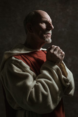 Fototapeta na wymiar Side view portrait of wishing monastic. Studio shot against dark