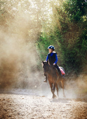 A young girl riding her pony during riding lesson, outside. Natural sun rays shining in dust during...