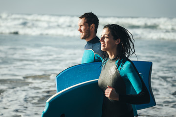 Young couple of bodyboard surfers runnign. Surfing and outdoor sport lifestyle concept. Woman and man after bodyboarding.