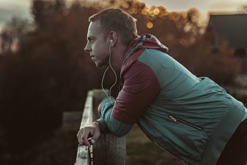 Attractive young athletic man standing on the beach and looks into  distance of  river to bridge, listening music.