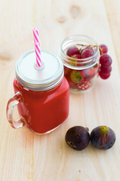 Strawberry juice, figs and grapes on wooden background.