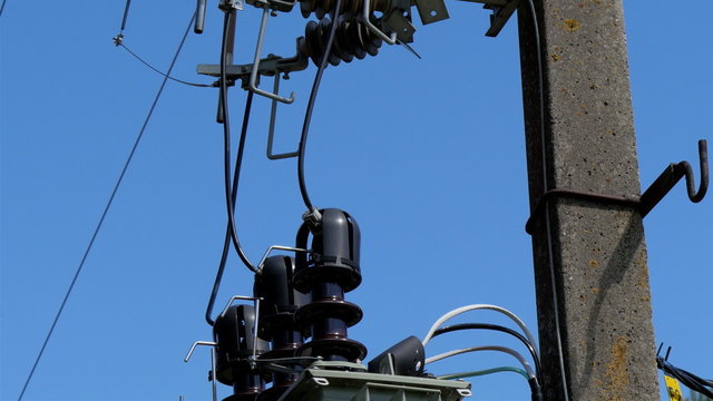 Big transformers and wires on the post. The electric posts is located on the side of a wide field with the blue sky