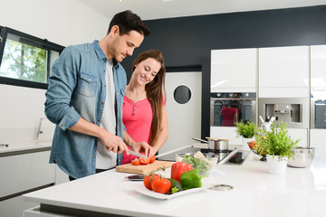 beautiful and happy young couple preparing organic vegetable salad together in kitchen at home