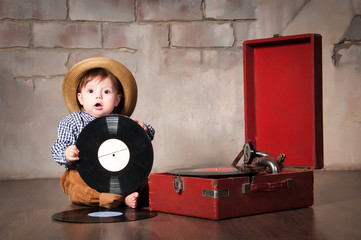 Funny baby boy in retro hat with vinyl record and gramophone