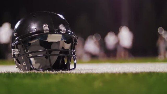 Close up of a football helmet on the field with a game going on in the background