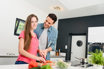 beautiful and happy young couple preparing organic vegetable salad together in kitchen at home