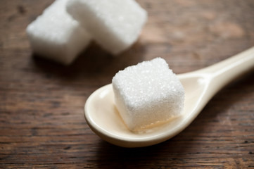 sucre en morceaux et petite cuillère beige sur fond en bois