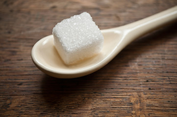 sucre en morceaux et petite cuillère beige sur fond en bois
