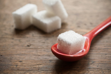 sucre en morceaux et petite cuillère rouge  sur fond en bois