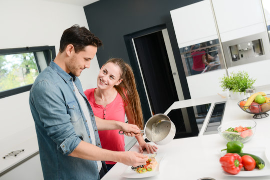beautiful and happy young couple having fun cooking together fresh food in kitchen at home