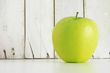 A green apple on a shelf against a white wooden wall. Empty copy space for editor's text.