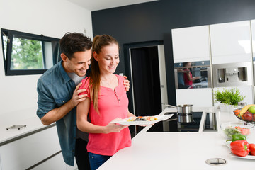 beautiful and happy young couple having fun cooking together fresh food in kitchen at home