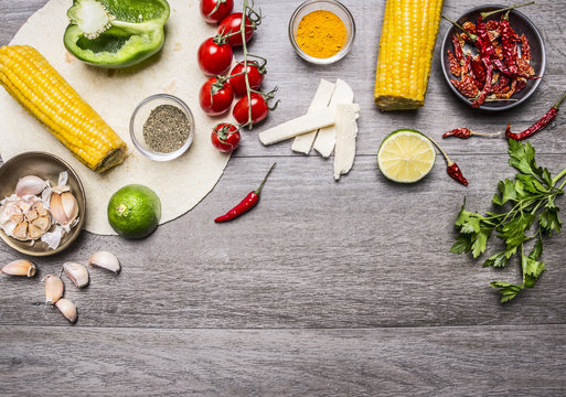 ingredients for burritos with tomato, pepper, spicy chili, corn, cheese and garlic border with space for text on grey wooden rustic background top view close up