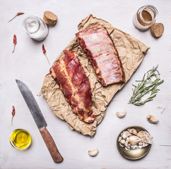 Ingredients for cooking double  raw lamb ribs on paper with a knife, garlic, salt, butter and herbs on white wooden rustic background top view