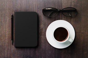Blank diary, pen, cup of coffee and glasses on dark brown wooden