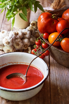 Close-up of a bowl of Tomato soup on a wooden table with fresh tomatoes, garlic and basil