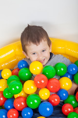 Fototapeta na wymiar Little smiling boy playing lying in colorful balls playground