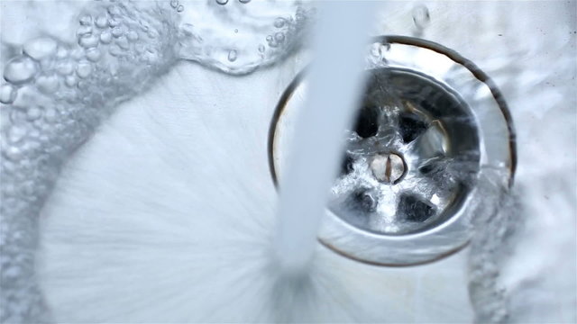 Water pouring into a stainless steel sink and running into the plug