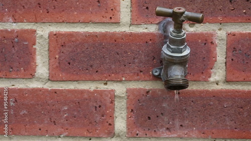 "Outside tap leaking water drips against a bright red ...