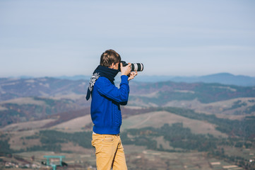 Man with a camera at the edge of a cliff overlooking the mountai