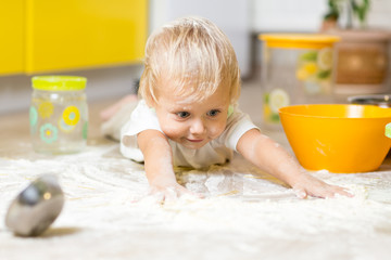 Little child laying on very messy kitchen floor, covered in white baking flour