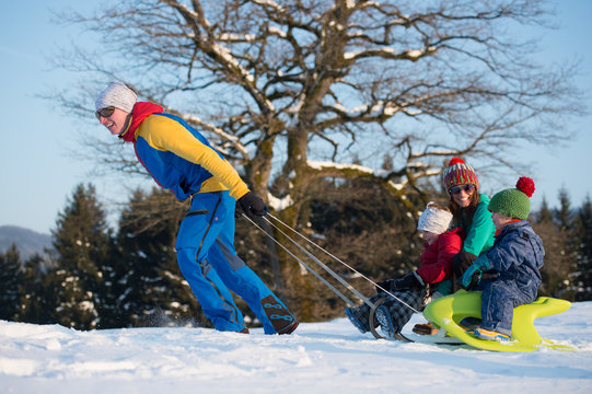 Junge Familie im Winter mit Kindern beim Schlittenfahren