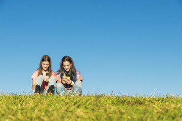 Two Teenage Girls Using Mobile In Park