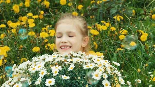 Closeup portrait girl and huge bouquet of white flowers. Child smiling at camera. Soap bubbles flying. Thumbs up. Ok
