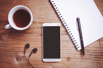 Smartphone with blank screen, earphones, notebook on wooden background ( Space and composition for text )