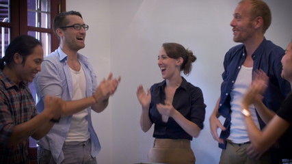 A mixed multi ethnic casual diverse group of young millennials in the workplace celebrate in a team cheer by putting their hands together at a job well done