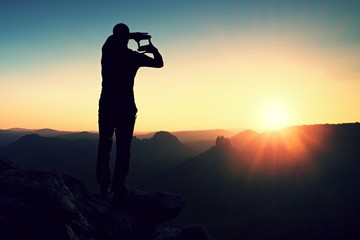 Tourist make frame with palms and fingers on both hands. Hiker on rocky cliff, daybreak in rocky mountains.