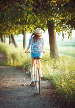 Girl in a hat riding a bicycle in a park - view from the back