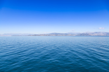 Obraz premium Blue sea waters and clear blue sky with distant land