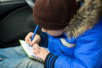 Boy writes in notebook sitting inside the car
