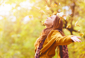 Beautiful young woman throwing leaves in a park, enjoying 