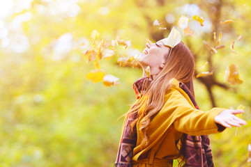 Beautiful young woman throwing leaves in a park, enjoying 
