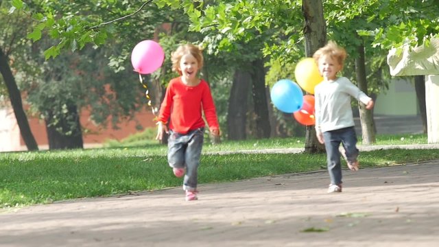 A smiling two little sisters with balloons running in the park, Slow motion