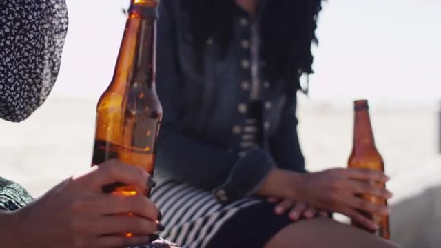 Close up of bottle of beer being held by woman talking to her friend