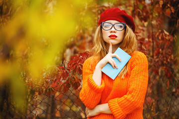 Lovely girl in beret and sweater in autumn park, holding noteboo