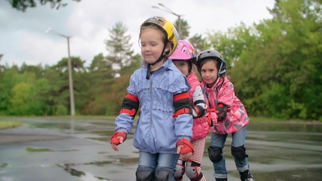 Three little girls wearing rollerblades skating in a row in slow motion 