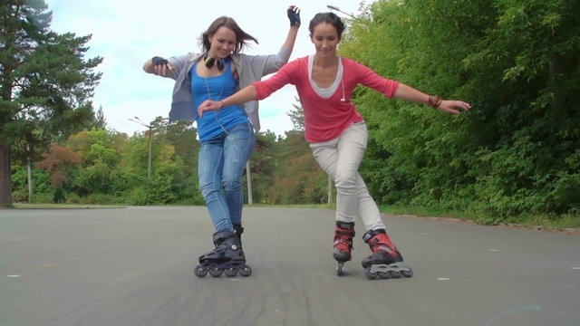 Two cheerful girls rollerblading together and doing a trick with crossed legs in super slow-motion