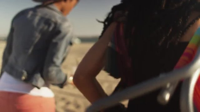 Close up handheld shot following two women friends across beach toward the ocean