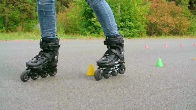 Legs of skilled inline skater doing freestyle activity around the cones