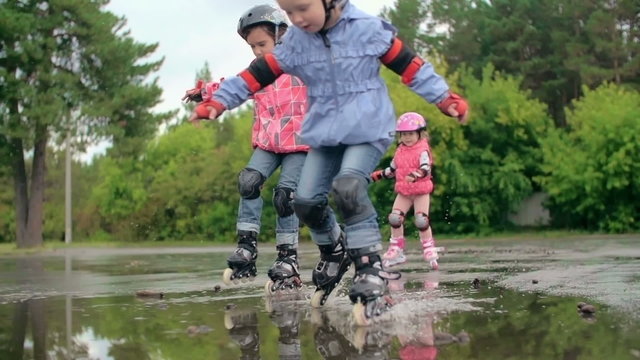 Slow motion shot of kids skating through puddles and splashing water 