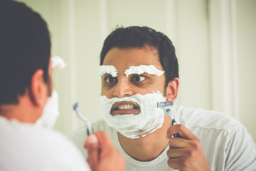 Closeup portrait, overzealous mentally deranged, mad as a hatter, young man at the end of his rope, attempting to shave his face eyebrows and face, isolated window reflection