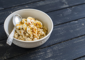 oatmeal with banana, caramel sauce and pecan nuts in a white bowl on a dark wooden surface, a delicious and healthy Breakfast