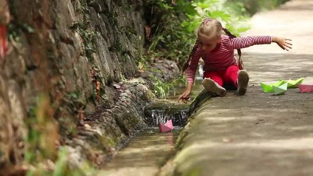 Girl is launching a toy-ship floating along the stream