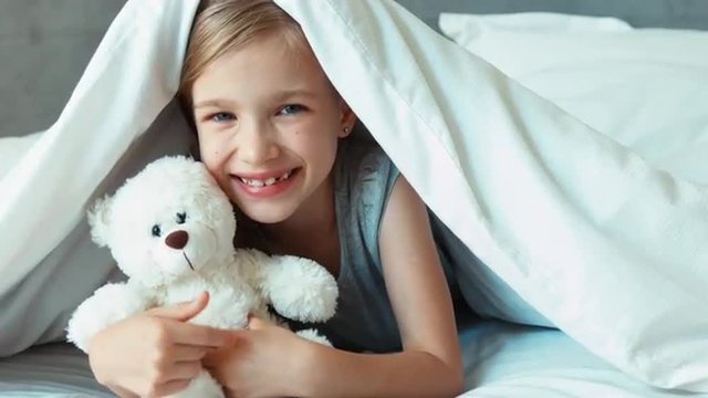 Girl kissing teddy bear. Child is under the blanket. Zooming