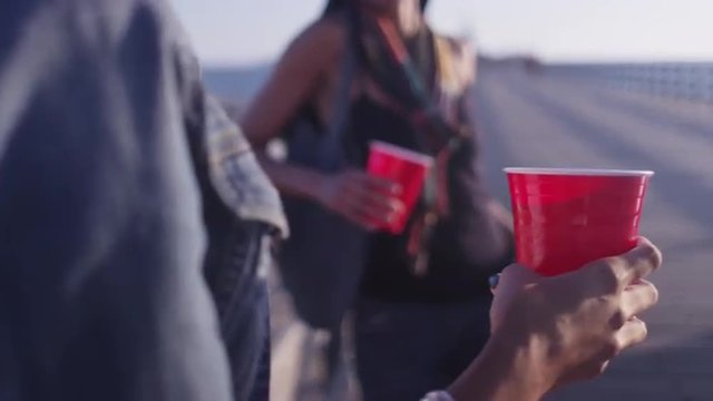 Close up of red plastic cups being held by two women friends leaning against wooden railing