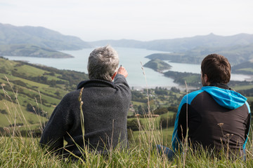 Two men sit on the top of hill and look at harbour, view from be